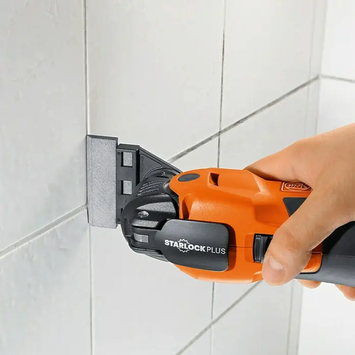 Fein Starlock Plus Set de limpieza de juntas de baldosas - 2 ud., Apto para: Cualquier anchura de junta - Herramienta oscilante Fein Multimaster en acción cortando azulejos. La herramienta naranja con montura Starlock Plus asegura resultados precisos.