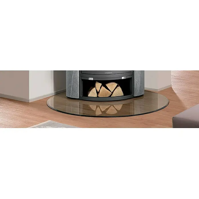 Justus Glasbodenplatte B7 - 110 x 110 cm, Tropfen - Der Kaminofen steht auf einer runden Glasplatte und bietet Platz für Holzscheite, eine elegante und praktische Ergänzung für jedes Wohnzimmer.