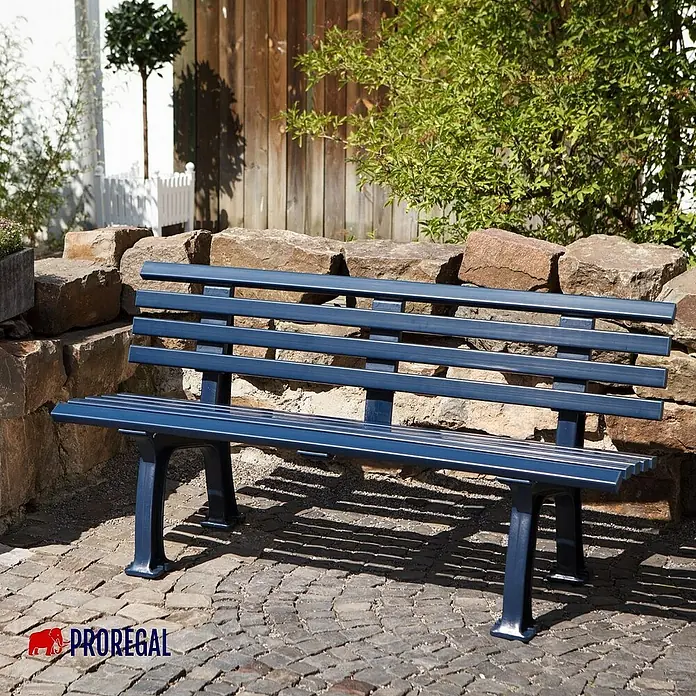 Proregal Gartenbank Antigua 3-Sitzer aus Kunststoff - Blau - Eine dunkelblaue Parkbank aus Metall und Holz steht vor einer Steinmauer und Grünpflanzen. Ideal für Parks und Gärten.