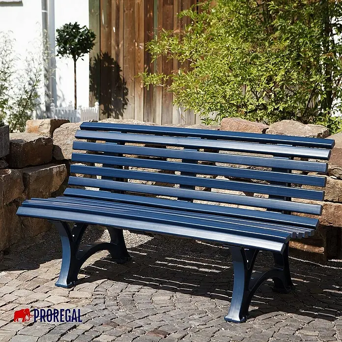 Proregal Gartenbank Jamaika 3-Sitzer aus Kunststoff - Blau - Eine blaue Parkbank aus Metall mit Lattenrost vor einer Steinmauer, ideal für den Garten oder Park.