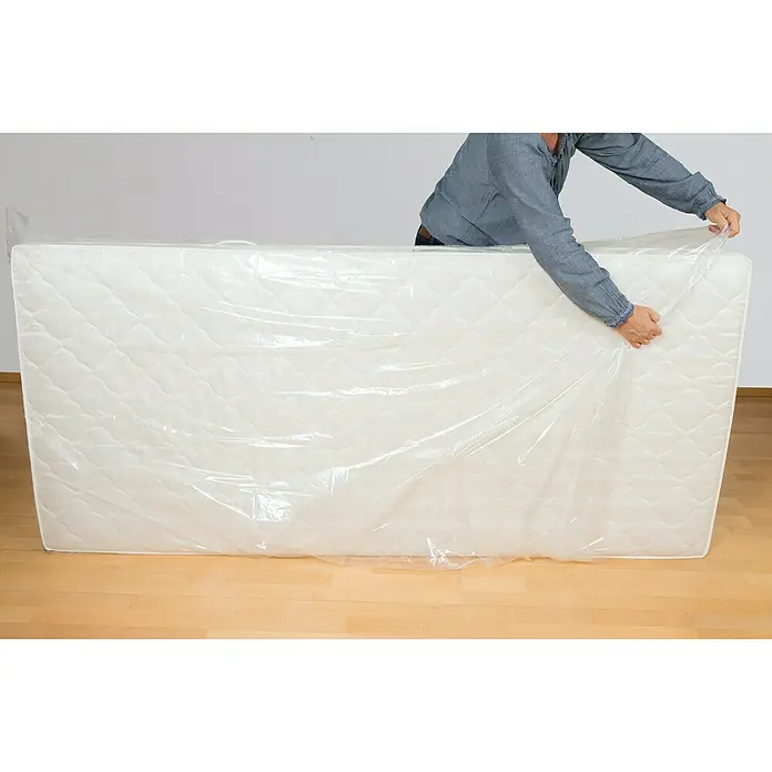 Matratzenhülle - 240 x 130 cm, Transparent, 2 Stk. - Person verpackt eine weiße Matratze in eine transparente Schutzfolie, um sie sauber und geschützt zu halten.