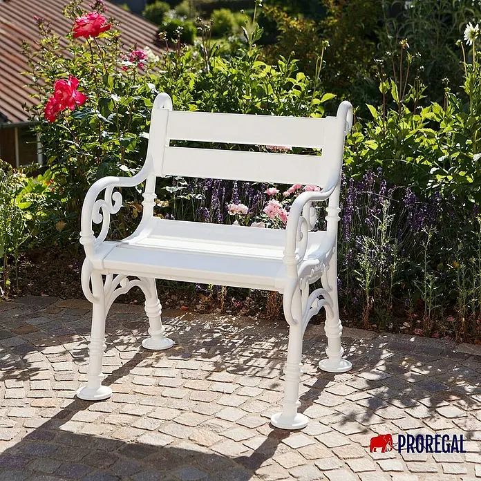 Proregal Gartenbank Curacao 1-Sitzer aus Kunststoff - Weiß - Elegante, weisse Gartenbank aus Metall. Die Bank steht auf einem gepflasterten Untergrund vor üppigem Grün.