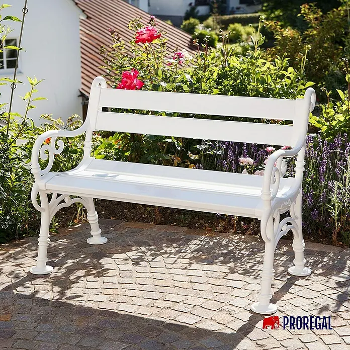 Proregal Gartenbank Curacao 2-Sitzer aus Kunststoff - Weiß - Eine elegante, weiße Gartenbank aus Metall mit dekorativen Verzierungen steht vor einem grünen Hintergrund.