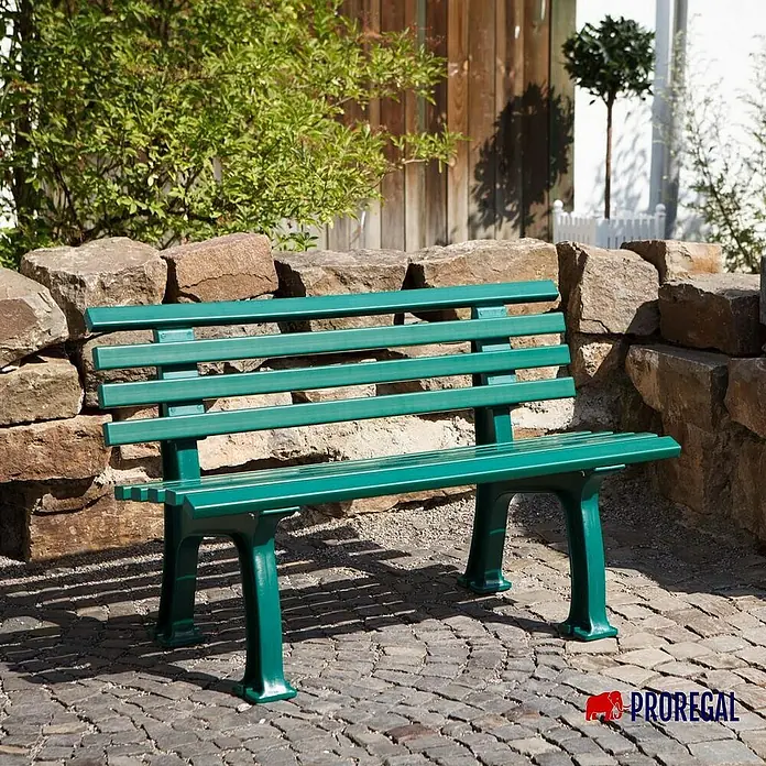 Proregal Gartenbank Antigua 2-Sitzer aus Kunststoff - Grün - Grün gestrichene Parkbank aus Holz mit Metallfüßen, die vor einer Steinmauer und einem Holzzaun steht.