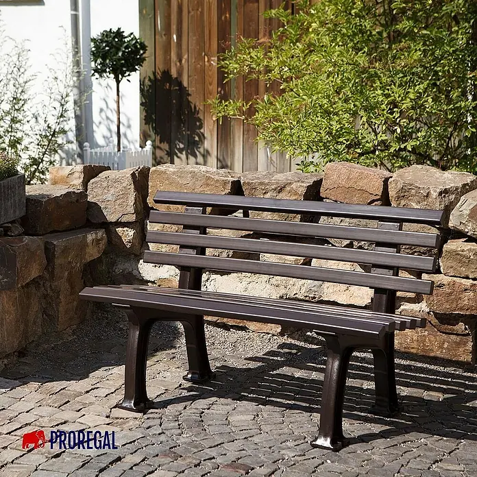 Proregal Gartenbank Antigua 2-Sitzer aus Kunststoff - Braun - Eine elegante, dunkelgraue Parkbank mit Lattenrost steht vor einer steinernen Mauer.