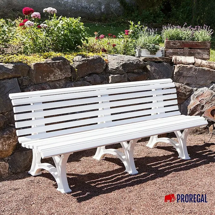 Proregal Gartenbank Jamaika 4-Sitzer aus Kunststoff - Weiß - Eine elegante, weiße Gartenbank vor einer Steinmauer mit Blumenbeeten. Die Bank lädt zum Verweilen im Grünen ein und bietet einen stilvollen Sitzplatz.