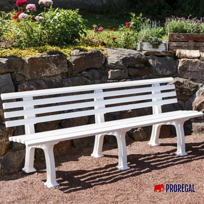 Proregal Gartenbank Antigua 4-Sitzer aus Kunststoff - Weiß - Weiße Gartenbank aus Kunststoff vor einer Steinmauer mit Blumenbeeten, die zum Entspannen im Freien einlädt.