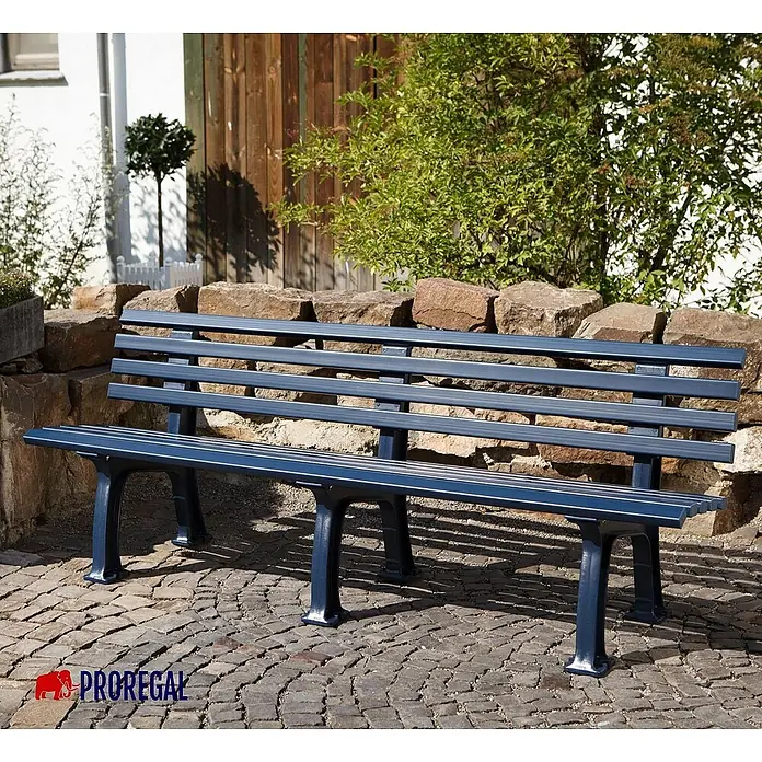 Proregal Gartenbank Antigua 4-Sitzer aus Kunststoff - Blau - Eine blaue Parkbank mit Metallrahmen steht vor einer Steinmauer und Grünpflanzen. Perfekt für Gärten oder öffentliche Plätze.