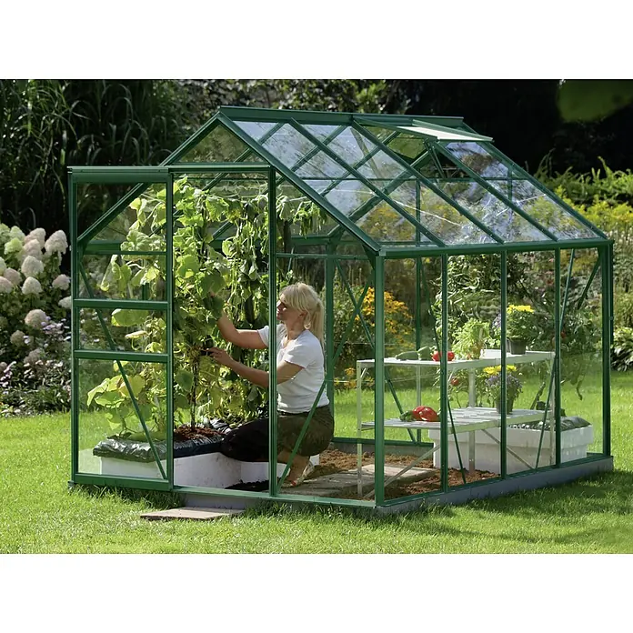 Vitavia Gewächshaus Venus 5000 Plus - Außenmaß inkl. Dachüberstand (B x T): 195 x 257 cm, 3 mm, Smaragd - Ein grünes Gewächshaus mit einer Frau darin, die sich um die Pflanzen kümmert. Das Gewächshaus ist aus Glas und Metall gefertigt.