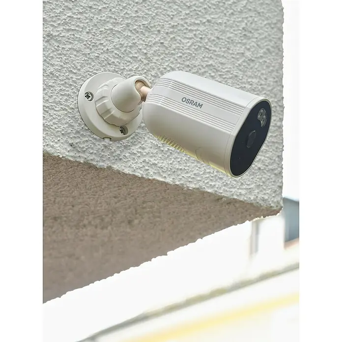 Osram Smart+ Überwachungskamera Outdoor Fixed - Passend für: Alarmsystem, Smart Home System - Nahaufnahme einer weißen Osram-Überwachungskamera, die an einer strukturierten Wand montiert ist und auf den Außenbereich gerichtet ist.