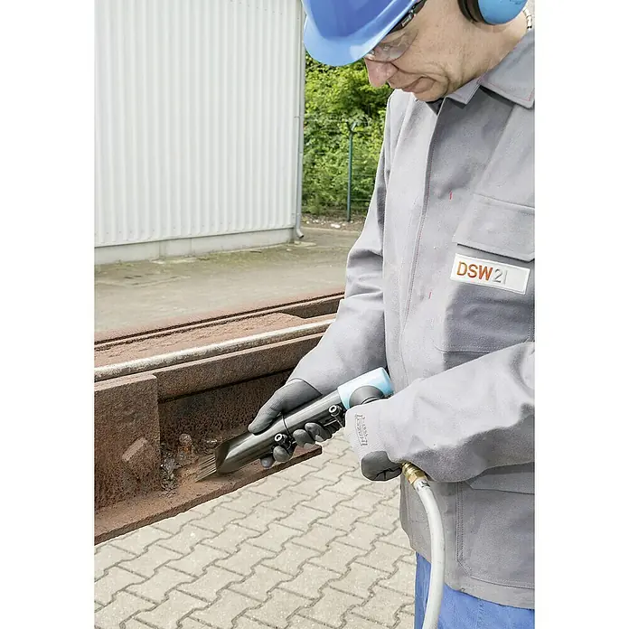 Hazet Nadelentroster 9035-5 - Betriebsdruck: 6,3 bar, Luftverbrauch: 170 l/min - Ein Arbeiter mit Schutzhelm und Gehörschutz, der mit einem Hazet Nadelluftschleifer Rost von einem Metallträger entfernt.