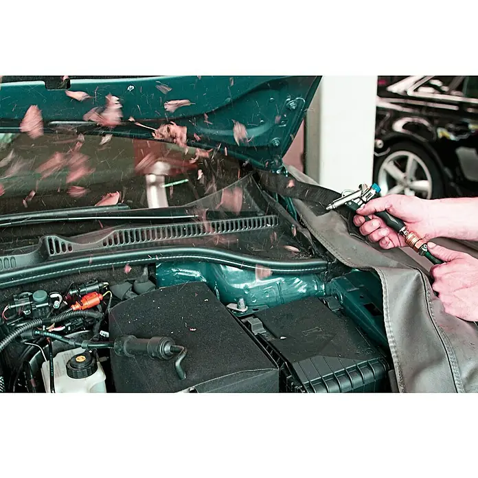 Hazet Ausblaspistole 9040-4Betriebsdruck: 6,3 bar, Durchflussmenge: 330 l/min - Das Bild zeigt die Motorraumreinigung eines Autos mit einer Sprühpistole, wobei eine Schutzdecke verwendet wird, um andere Bereiche zu schützen.