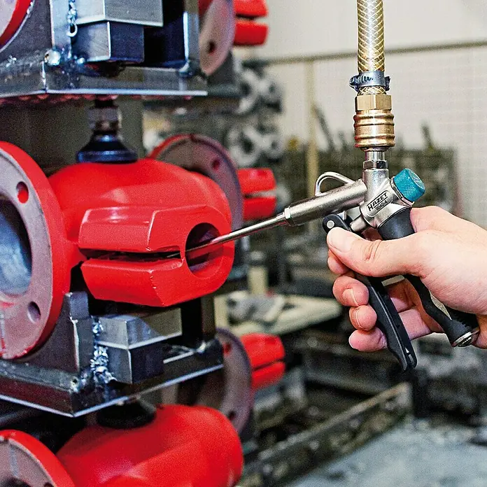 Hazet Ausblaspistole 9040-4 - Betriebsdruck: 6,3 bar, Durchflussmenge: 330 l/min - Ein HAZET 9040-4 Druckluftpistole wird verwendet, um ein rotes Metallteil zu reinigen. Das Werkzeug ist mit einem Schlauch verbunden.