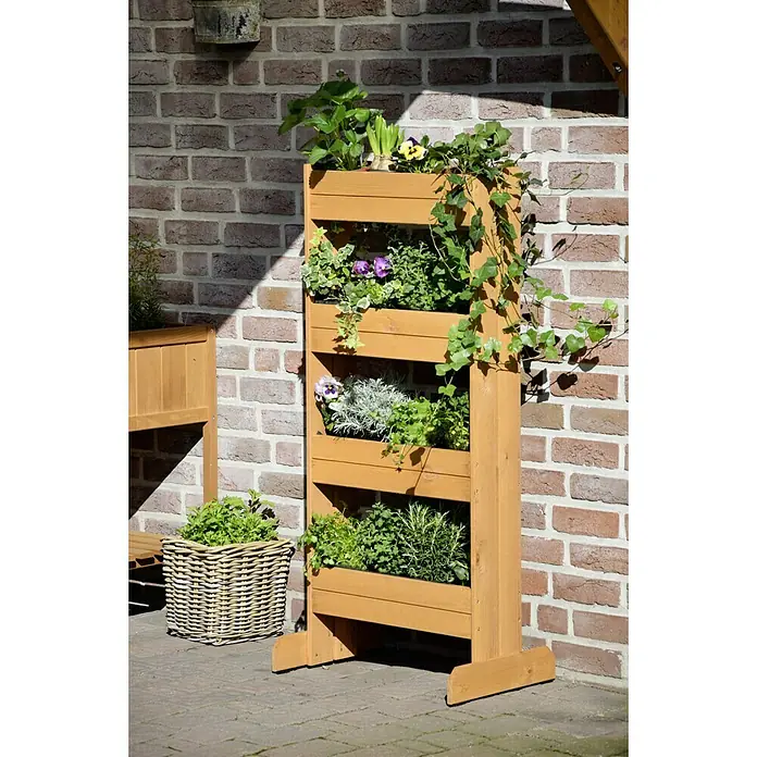 Dobar Hochbeet - 55 x 40 x 125 cm, Holz, Bernstein - Mehrstöckiges Pflanzenregal aus Holz mit verschiedenen Pflanzen, darunter Blumen und Kräuter, vor einer Backsteinmauer.