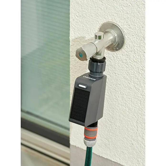 Osram Smart+ Bewässerungssteuerung - Batteriebetrieben, Passend für: Bewässerungssteuerung, Smart Home System, 1 & ¾ Zoll Wasserhahn - Nahaufnahme eines Wasserhahns mit angeschlossenem smarten Bewässerungsgerät von Osram. Das Gerät hat ein Solarpanel zur Stromversorgung.