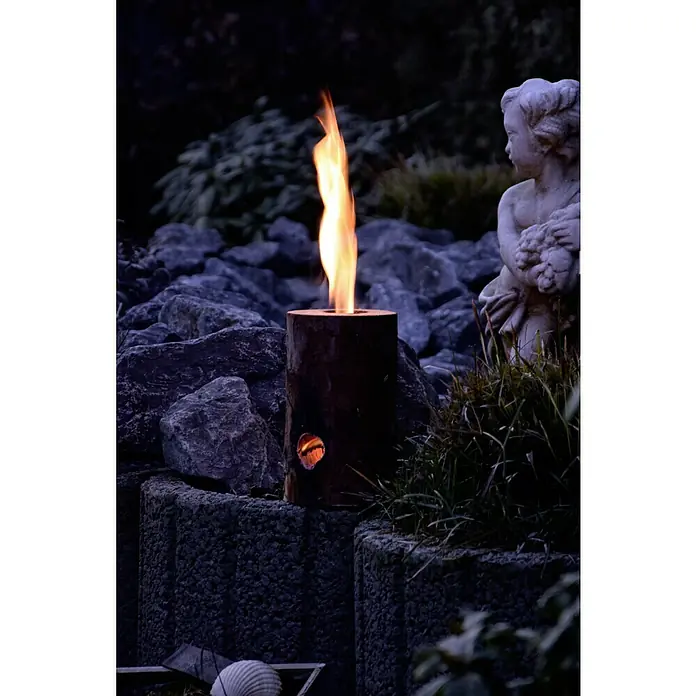 Dobar Schwedenfeuer Set - 11 cm - 15 cm - Holzofen mit loderndem Feuer und einer Öffnung für die Luftzufuhr, platziert auf einem Steinsockel neben einer Engelstatue.