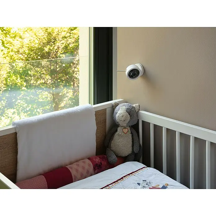 Osram Smart+ Überwachungskamera Fixed - Passend für: Alarmsystem, Smart Home System - Eine Nahaufnahme eines Kinderbetts mit einer Überwachungskamera an der Wand, die für Sicherheit sorgt. Der Teddybär sitzt am Rand.