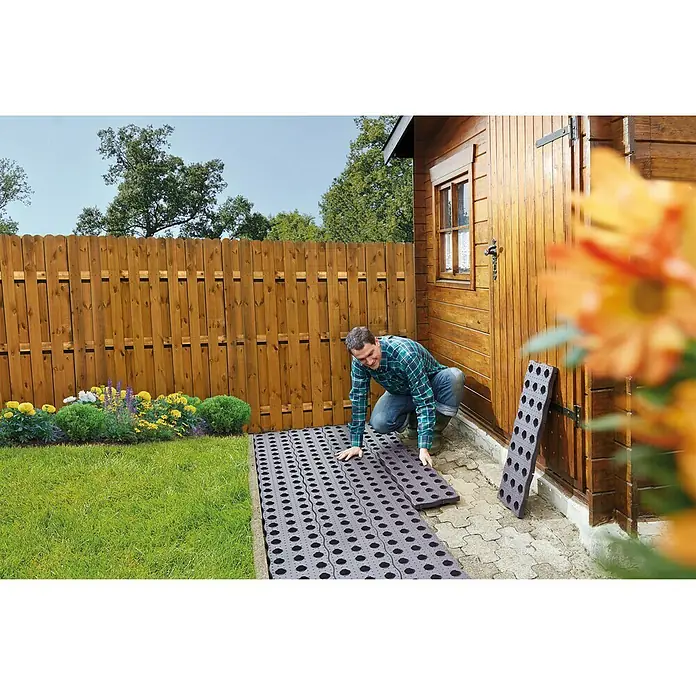 Garantia Beetplatte Maxi - 4 Stk., 70 x 24 cm - Ein Mann verlegt Gartenplatten aus Kunststoff mit runden Löchern, um einen Weg zu gestalten. Die Platten sind leicht und einfach zu verlegen.
