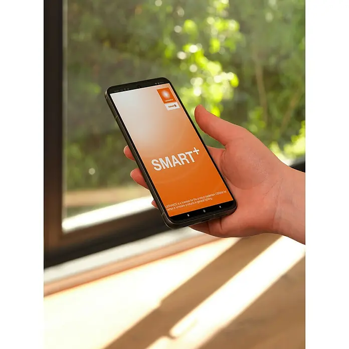 Osram Smart+ Überwachungskamera Fixed - Passend für: Alarmsystem, Smart Home System - Nahaufnahme eines Smartphones mit der LEDVANCE SMART+ App auf dem Bildschirm, gehalten in einer Hand vor einem Fenster.