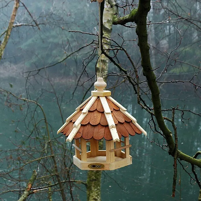 Dobar Vogelhaus - 33 x 29 x 36 cm, Natur/Braun - Ein hölzernes Vogelhaus mit einem braunen Schindeldach hängt an einem Baum vor einem trüben Hintergrund.