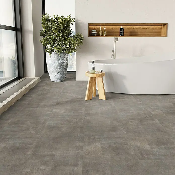 Parador Vinylbodenmuster Basic 5.3 Mineral grey - 200 x 457 x 5,3 mm, Fliesenoptik - Ein modernes Badezimmer mit grauen Fliesen, einer freistehenden Badewanne und einem Holzhocker mit Badutensilien.