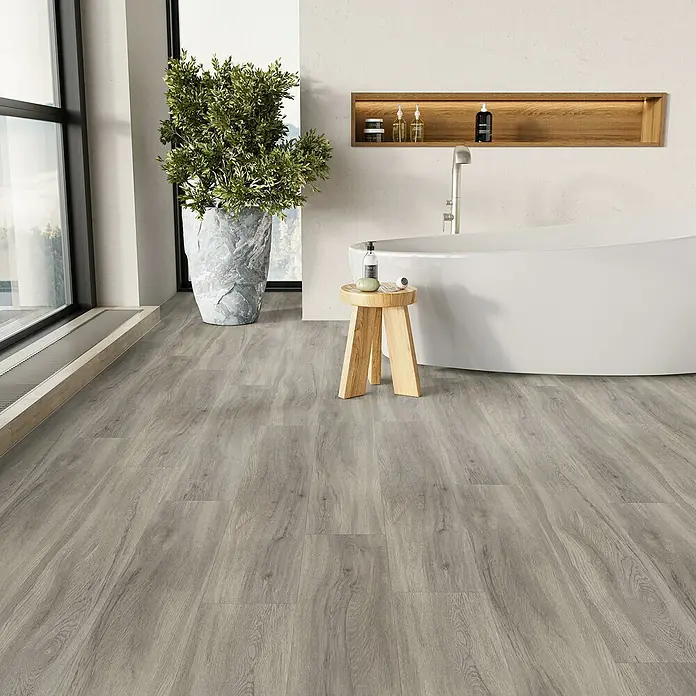 Parador Vinylboden Basic 5.3 - Eiche pastellgrau, Landhausdiele, 1.209 x 225 x 5,3 mm - Ein Badezimmer mit einem freistehenden Bad, einem Holzhocker und einer Pflanze, der graue Holzboden verleiht dem Raum Wärme und Textur.