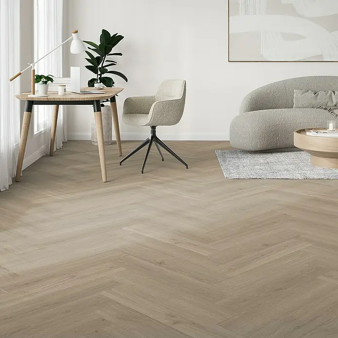 Parador Vinylboden Trendtime 3 - Eiche Regent grau, Fischgrät, 730 x 146 x 5 mm - Ein helles Interieur mit einem Schreibtisch, einem bequemen Stuhl und einem stilvollen Sofa auf einem warmen Holzboden.