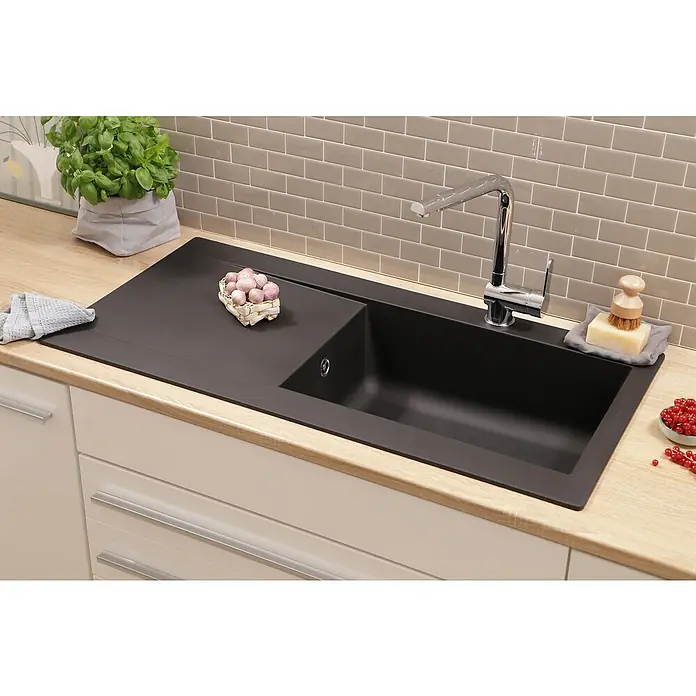 Respekta Einbauspüle Denver - 50 x 100 cm, Anzahl Becken: 1 Stk., Schwarz - Elegante schwarze Spüle mit Abtropffläche, Hahn, Seife, Bürste und Knoblauch auf einer hellen Arbeitsplatte vor grauen Fliesen.