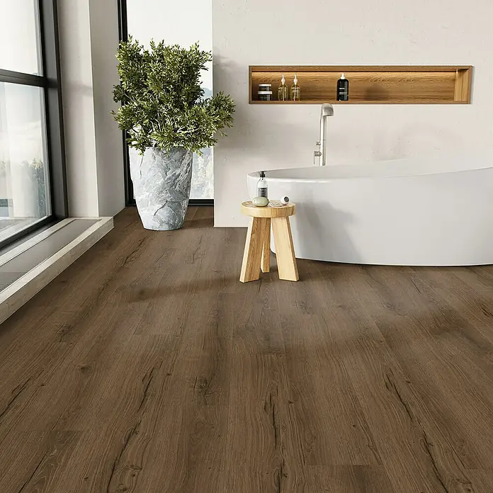 Parador Vinylboden Basic 5.3 - Eiche Cambridge geräuchert, Landhausdiele, 1.209 x 225 x 5,3 mm - Ein Badezimmer mit hellen Wänden und einem dunklen Holzboden. Eine freistehende Badewanne steht neben einem hölzernen Beistelltisch.