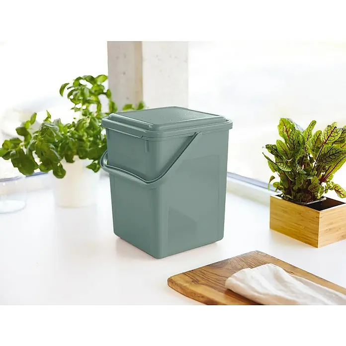 Proregal Standard-Mülleimer Robuster Abfalleimer mit geruchsdichtem Deckel - 9 l, Kunststoff, Grün - Ein grüner Komposteimer mit Deckel steht auf einer weißen Küchentheke, daneben Kräutertöpfe und ein Schneidebrett.