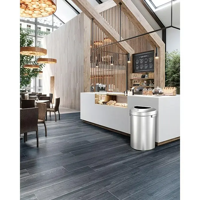 Proregal Standard-Mülleimer Stilvoller halbrunder offener Abfallsammler aus gebürstetem Edelstahl - 80 l, Edelstahl, Silber - Ein schlanker, silberner Mülleimer aus Edelstahl mit schwarzem Deckel steht in einem eleganten Café. Perfekt für stilvolle Abfallentsorgung.