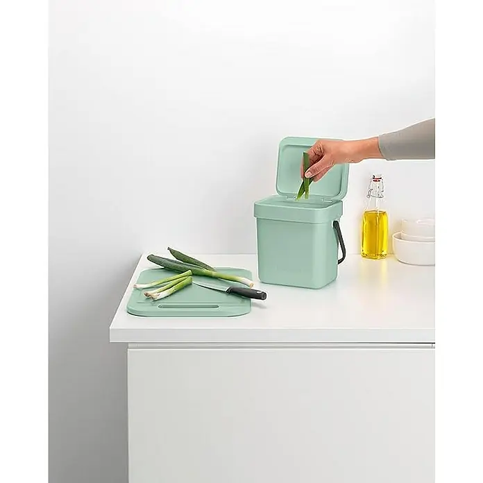 Proregal Standard Mülleimer Brabantia Abfallsammler mit Stay-open Deckel - 3 l, Kunststoff, Jade - Hellgrüner Bioabfalleimer mit Lebensmitteln und Schneidebrett auf einer Küchentheke.