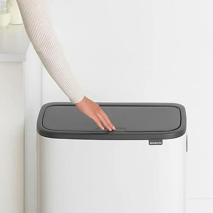 Proregal Sensormülleimer Brabantia Hochwertiger Abfallsammler mit Touch-Öffnung - 60 l, Metall, Weiß - Eine Hand öffnet den Deckel eines weißen, rechteckigen Brabatnia-Abfalleimers mit grauem Deckel vor einem hellen Hintergrund.