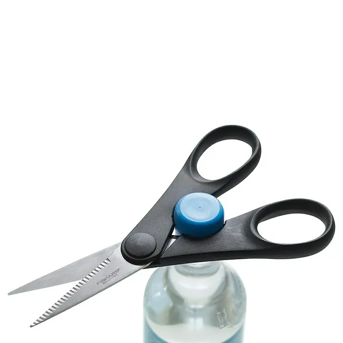 Fiskars Küchen-Schere - Länge: 21 cm - Eine Nahaufnahme einer Zickzackschere von Fiskars, die auf einer blauen Wasserflasche mit blauem Verschluss balanciert.