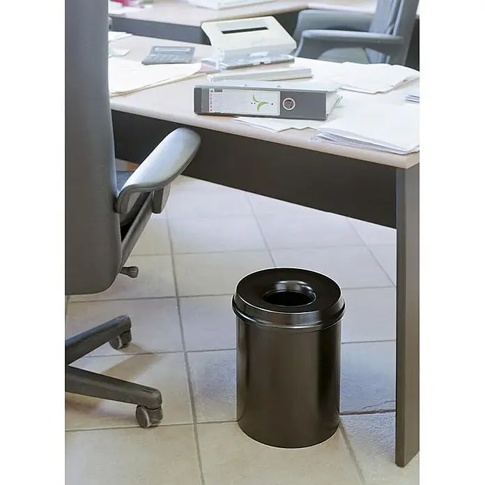Proregal Papierkorb & Abfallsammler aus Metall selbstlöschend - 30 l, Metall, Schwarz - Ein runder, schwarzer Abfalleimer aus Metall steht neben einem Bürostuhl unter einem Schreibtisch im Büro. Praktische Büroausstattung.