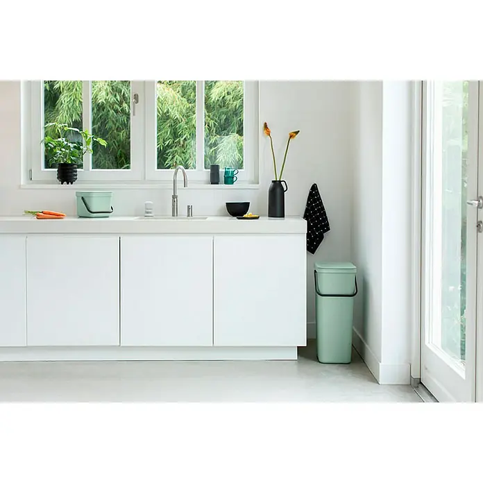 Proregal Standard-Mülleimer Brabantia Abfallsammler mit Stay-open Deckel - 6 l, Kunststoff, Jade - Ein mintgrüner Küchenmülleimer und ein kleinerer Kompostbehälter stehen in einer hellen, modernen Küche. Der große Eimer steht neben der Tür.