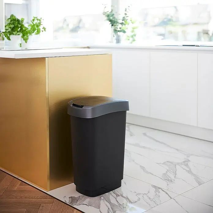 Proregal Standard Mülleimer Klassischer Abfalleimer für Innenbereich - 50 l, Kunststoff, Schwarz-Silber - Ein schwarzer Mülleimer mit grauem Deckel steht neben einer goldenen Kücheninsel, der sich perfekt in die moderne Kücheneinrichtung einfügt.