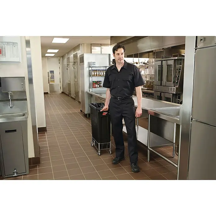Proregal Standard-Mülleimer Rubbermaid Slim Jim Mülleimer mit Belüftungskanälen - 87 l, Kunststoff, Schwarz - Ein Mann in Arbeitskleidung steht in einer Großküche neben einem schwarzen Müllwagen mit Rollen, professionelle Küchenausstattung.