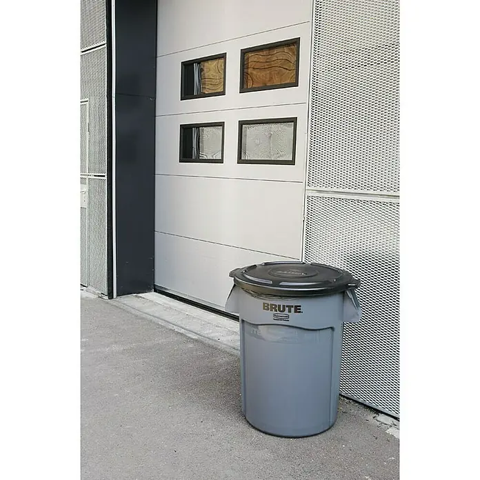 Proregal Standard-Mülleimer Rubbermaid Brute runde Mehrzwecktonne mit Belüftungskanälen - 75,7 l, Kunststoff, Grau - Graue "Brute" Mülltonne mit schwarzem Deckel vor einer weißen Garagentür, ideal für gewerbliche oder private Nutzung.