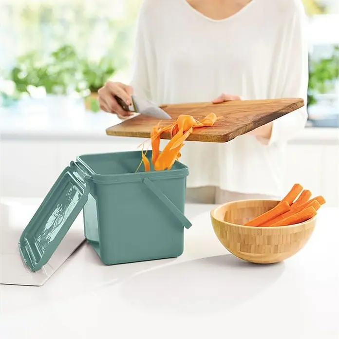 Proregal Standard Mülleimer Robuster Abfalleimer mit geruchsdichtem Deckel - 5 l, Kunststoff, Grün - Ein mintgrüner Komposteimer mit einem abnehmbaren Deckel, der für Küchenabfälle verwendet wird, während eine Person Gemüsereste entsorgt.
