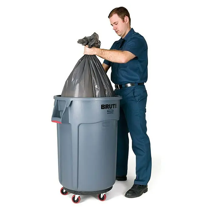 Proregal Standard-Mülleimer Rubbermaid Brute runde Mehrzwecktonne mit Belüftungskanälen - 166,5 l, Kunststoff, Grau - Ein Mann befüllt einen grauen, rollbaren "Brute"-Mülleimer mit einem schwarzen Müllsack. Der Mülleimer ist mit einem "Rubbermaid"-Logo versehen.