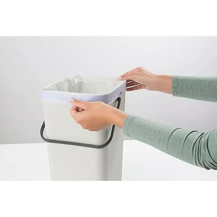 Proregal Standard Mülleimer Brabantia Abfallsammler mit Stay-open Deckel - 16 l, Kunststoff, Hellgrau - Eine Person befestigt eine Mülltüte an einem hellgrauen, rechteckigen Mülleimer mit schwarzem Griff, um die Hygiene zu gewährleisten.