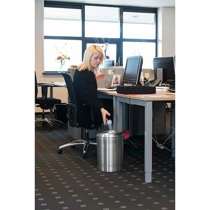 Proregal Papierkorb & Abfallsammler aus Aluminium selbstlöschend - 20 l, Aluminium, Silber - Eine blonde Frau wirft ein zerknittertes Papier in einen silbernen Mülleimer unter einem Schreibtisch in einem Büro.