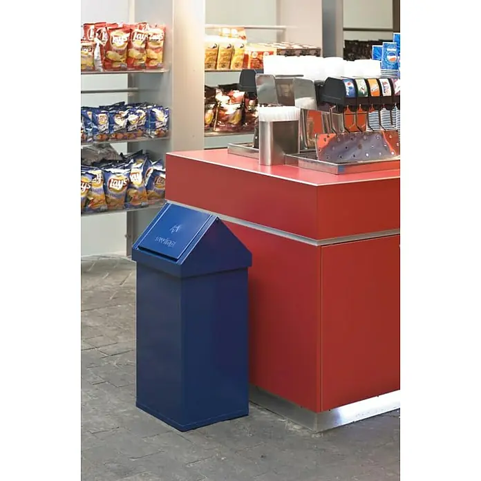 Proregal Standard Mülleimer Eckiger Aluminium Abfallbehälter Haiti mit Swingdeckel - 55 l, Aluminium, Blau - Das Bild zeigt einen blauen Abfallbehälter neben einem roten Tresen mit Getränkespendern und Regalen voller Snacks.