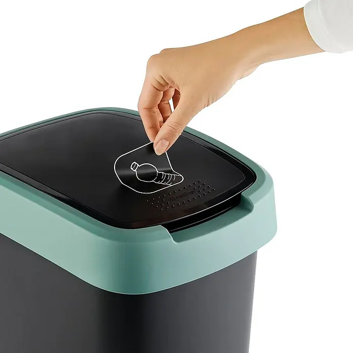 Proregal Standard-Mülleimer Klassischer Abfalleimer für Innenbereich - 25 l, Kunststoff, Schwarz-Grün - Ein Mülleimer mit einem grünen Deckel und einer Hand, die einen Aufkleber entfernt.