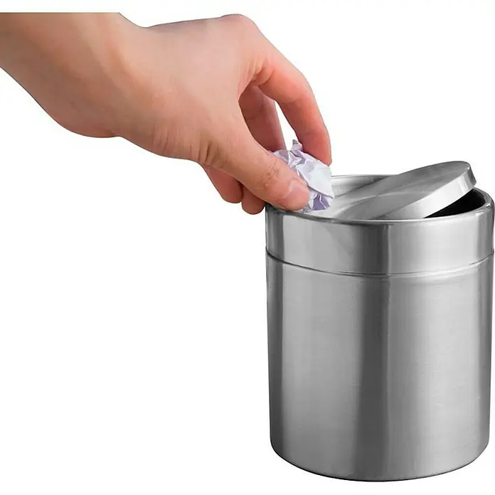 Proregal Schwingdeckeleimer Schön geformter Tischabfallbehälter mit Flachschwingdeckel - 1,5 l, Edelstahl, Edelstahl / Silber - Ein silberner, kleiner Mülleimer mit Schwingdeckel, in den eine Hand ein zerknittertes Papier wirft.