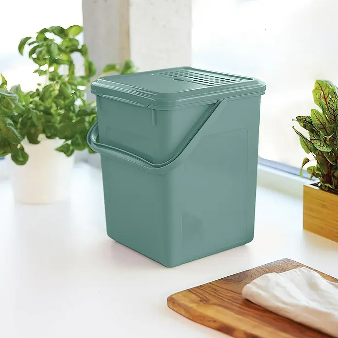 Proregal Standard-Mülleimer Robuster Abfalleimer mit geruchsdichtem Deckel & Kohlefilter - 9 l, Kunststoff, Grün - Eine mintgrüne Biotonne mit Deckel und Griff steht auf einer weißen Oberfläche, umgeben von Pflanzen und einem Schneidebrett.