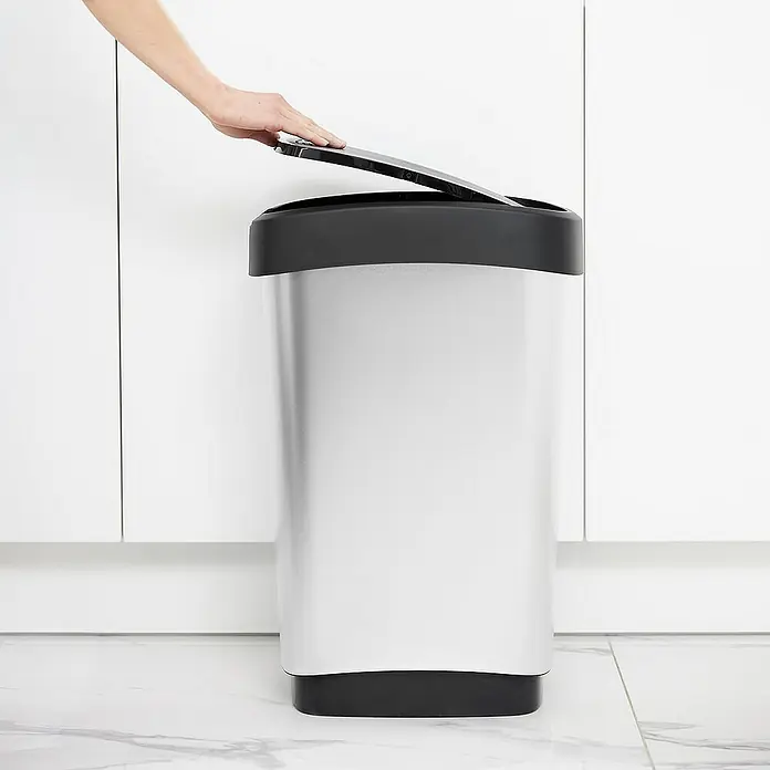 Proregal Standard Mülleimer Klassischer Abfalleimer für Innenbereich - 50 l, Kunststoff, Silber-Schwarz - Ein silberfarbener Mülleimer mit schwarzem Deckel wird von einer Hand geöffnet, stehend auf einem Marmorboden vor weißen Schränken.