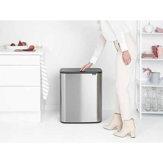Proregal Sensormülleimer Brabantia Hochwertiger Abfallsammler mit Touch-Öffnung - 60 l, Edelstahl, Edelstahl - Eine Frau öffnet einen silberfarbenen, rechteckigen Mülleimer von Brabantia in einer hellen Küche. Der Mülleimer hat einen schwarzen Deckel.
