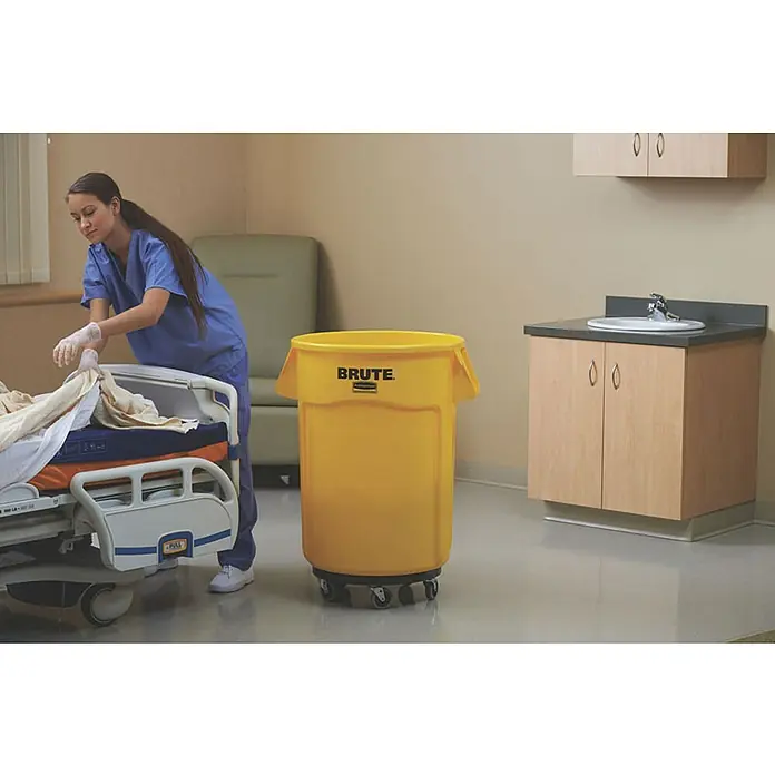 Proregal Standard-Mülleimer Rubbermaid Brute runde Mehrzwecktonne mit Belüftungskanälen - 166,5 l, Kunststoff, Gelb - Das Bild zeigt einen gelben Brute-Abfallbehälter mit Rollen in einem Krankenhauszimmer, neben einem Krankenbett und einem Waschbecken.